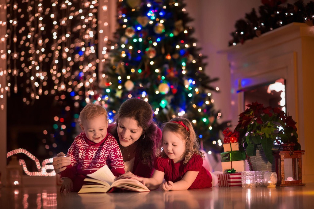 Mãe lendo histórias com os filhos ao pé da árvore de Natal iluminada